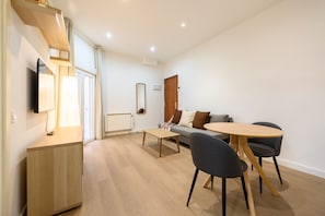 Ein modernes Wohnzimmer mit einer Couch, einem runden Tisch und einem Fernseher auf einem Holzständer.
