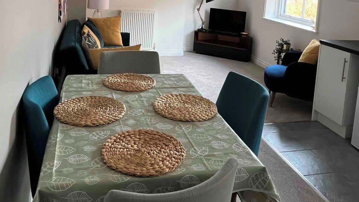 A dining area with a table set with woven placemats, surrounded by chairs.