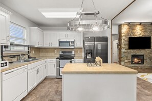 A modern kitchen with white cabinets, stainless steel appliances, a central island, and a stone fireplace. - Cozy Retreat with Porch Swing Near Houston ~ Stylish (Richmond)