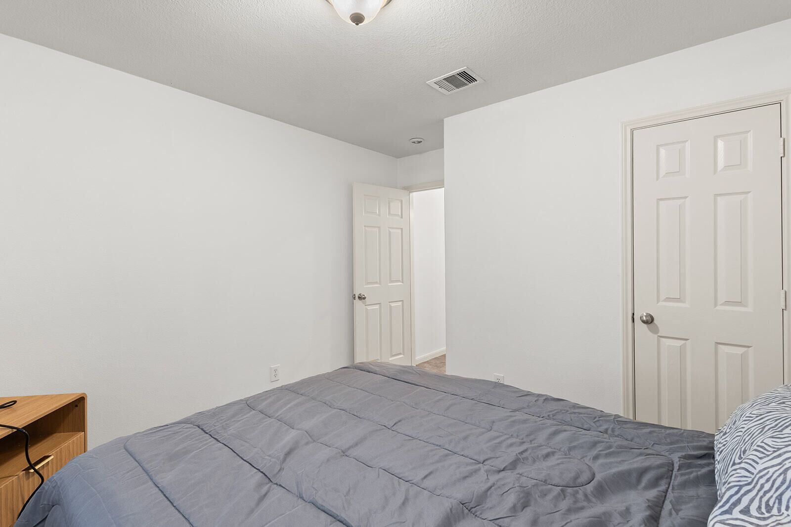 Een slaapkamer met een bed, een houten nachtkastje, een witte deur en een wit plafond.