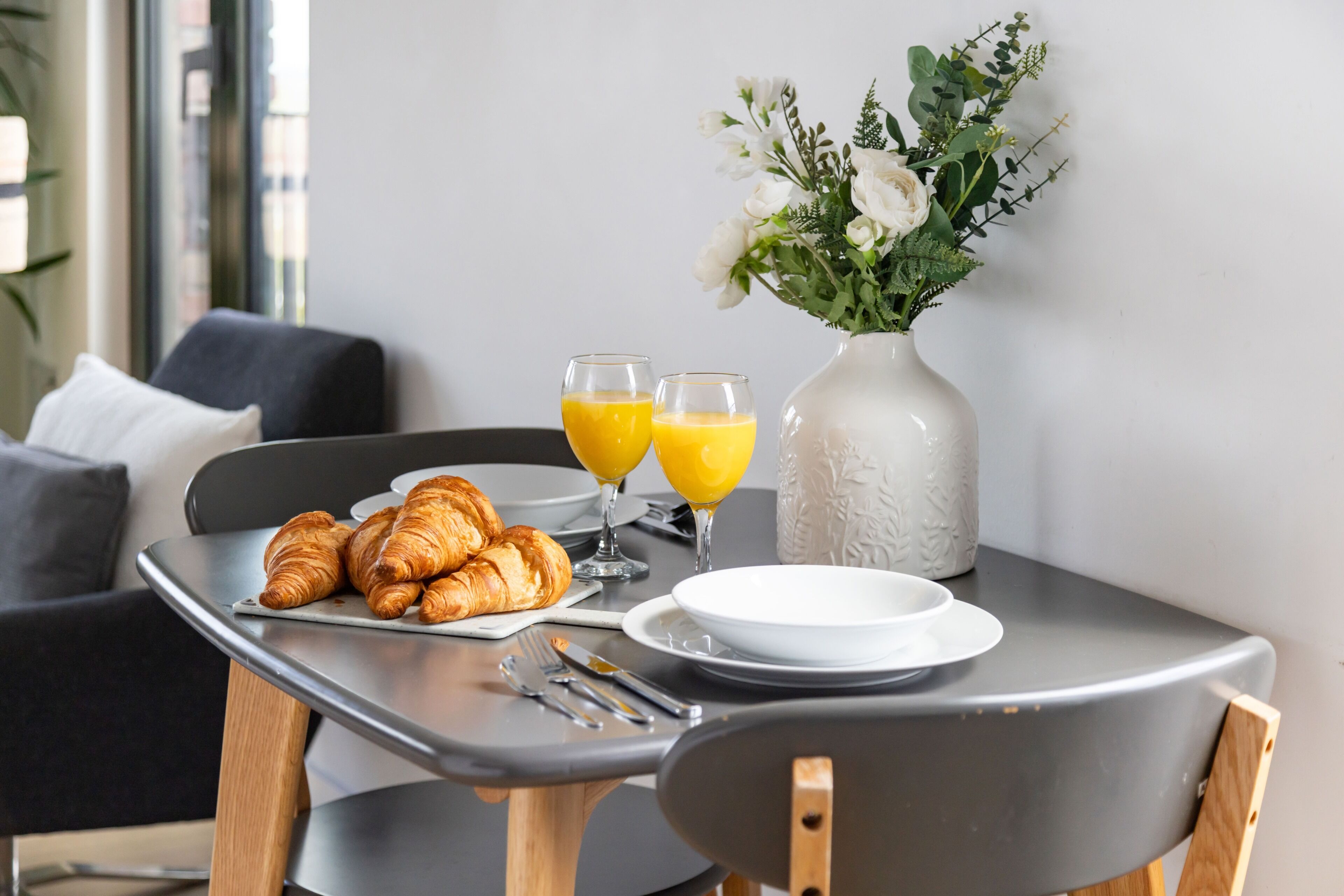 Ein Frühstückstisch mit Croissants, Orangensaft und einer Blumenvase.
