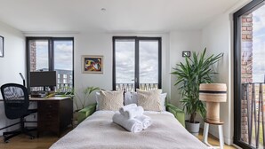 A modern bedroom with a large bed, a desk, and a view of the sky through the windows. - Modern 1BR Kings Cross Hideaway (London)