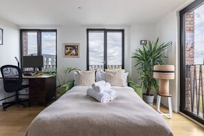 Ein modernes Schlafzimmer mit einem großen Bett, einem Schreibtisch und Blick zum Himmel durch die Fenster.