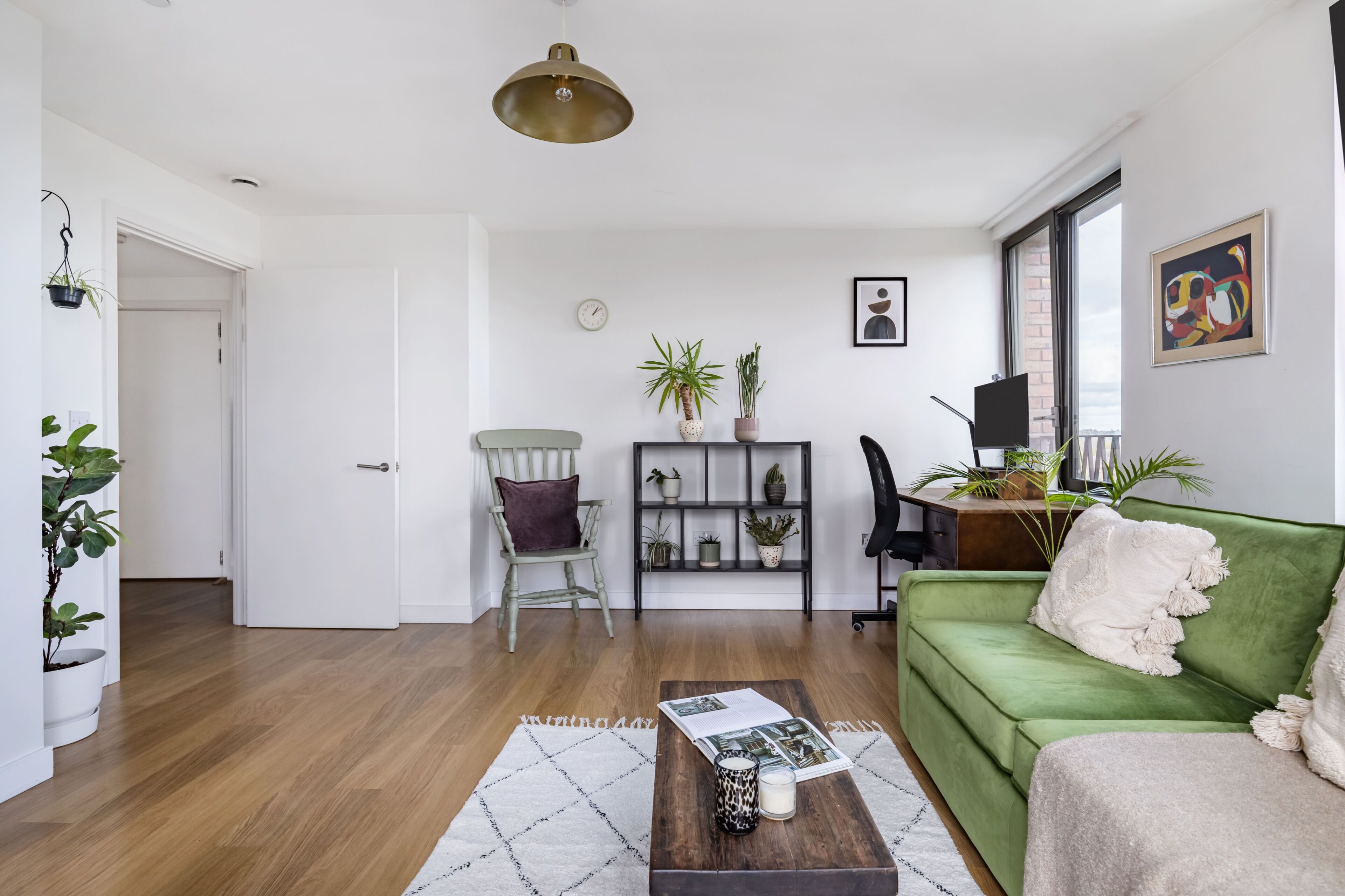 Un salon avec un canapé vert, une table basse en bois, un fauteuil, une bibliothèque et un téléviseur.