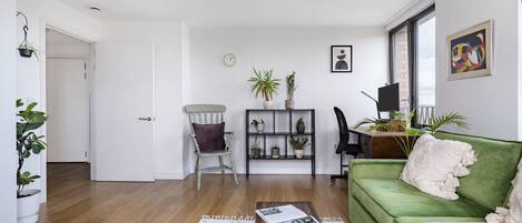 Un salon avec un canapé vert, une table basse en bois, un fauteuil, une bibliothèque et un téléviseur.