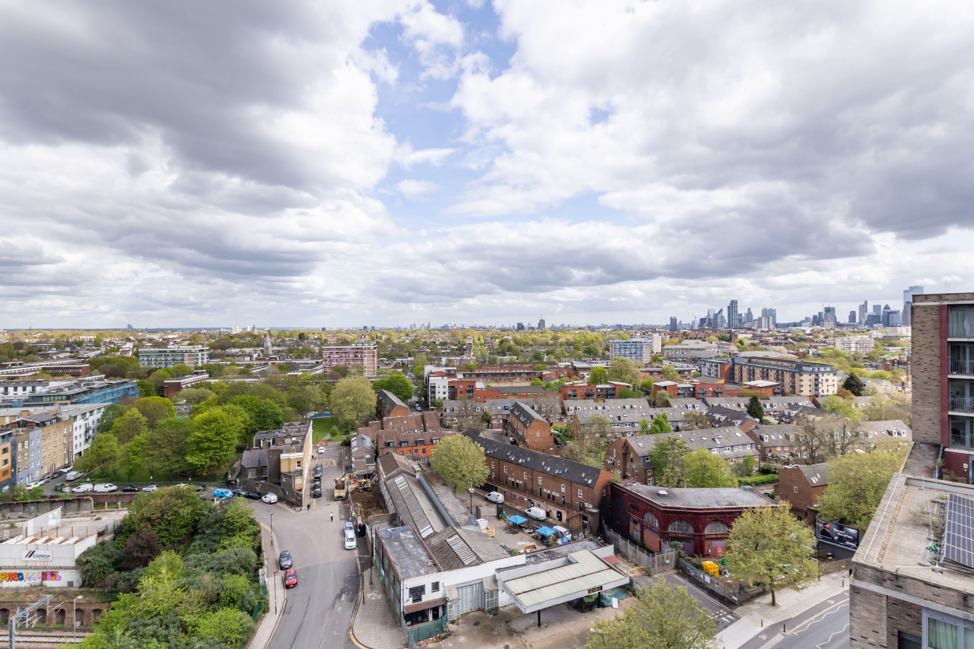 A cityscape with a mix of residential and commercial buildings, a clear sky, and a distant view of a city skyline.