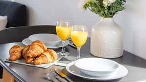 A breakfast table with croissants, orange juice, and a vase of flowers. - Modern 1BR Kings Cross Hideaway (London)