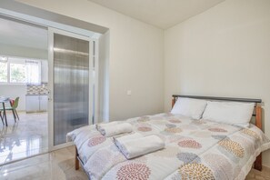 Une chambre avec un lit, une porte-fenêtre coulissante donnant sur un balcon et une petite kitchenette.