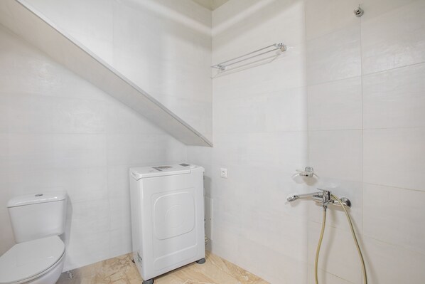 A bathroom with a toilet, a washing machine, and a shower.