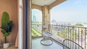 Een balkon met een hangstoel, een bloempot en uitzicht op een stadsgezicht met gebouwen en een brug.