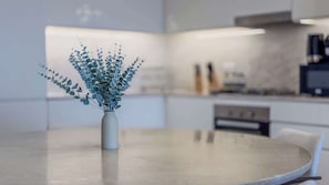 A modern kitchen with a round table, a vase with greenery, and a blurred background. - Waterfront Luxury | Furnished | Full Creek View (Dubai)