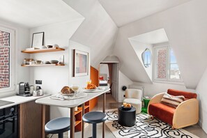 A modern loft apartment with a kitchen, dining area, and living space, featuring a sloped ceiling, exposed brick walls, and large windows. - Stylish 1BR Parc Monceau Retreat (Paris)