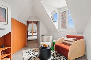 A loft-style room with a sloped ceiling, a rattan chair, a red sofa, and a view of the sky through a window. - Stylish 1BR Parc Monceau Retreat (Paris)