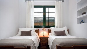 A bedroom with two single beds, a nightstand with a lamp, a window with curtains, and a shelf with decorative items. - El Secreto de las Eras - Charming rural house in Candelario, nature (Candelario)