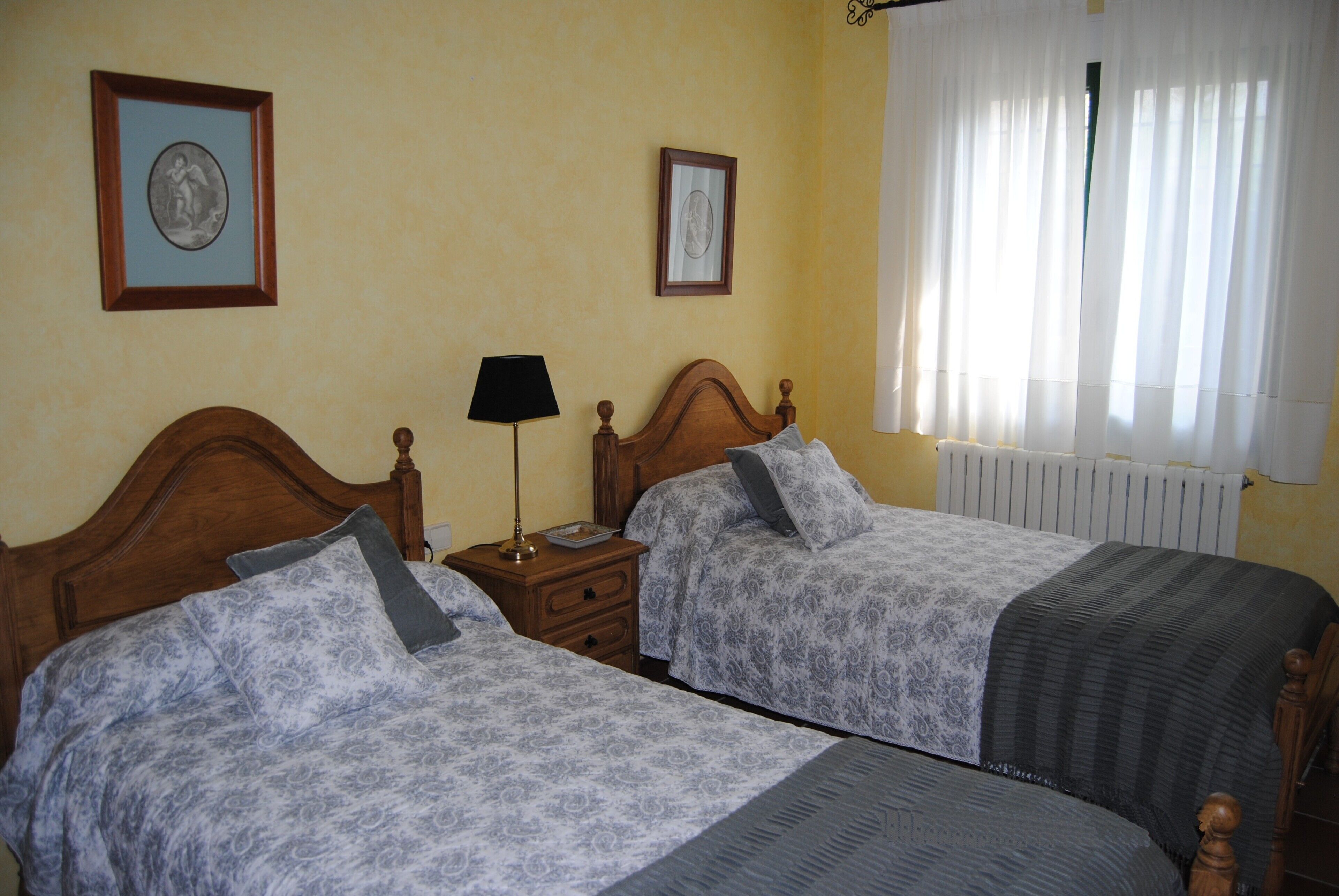 Una habitación de hotel con dos camas, una mesita de noche con lámpara y dos cuadros en la pared.