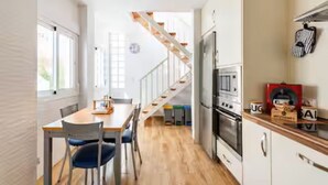 Eine kleine Küche mit einer Holztreppe, einem Essbereich mit Stühlen und einem Kühlschrank.