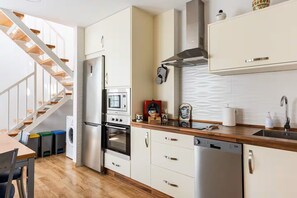 A kitchen with a built-in oven, microwave, and dishwasher, a wooden staircase, and a white tiled backsplash. - Spacious and bright apartment with large private roof terrace-solarium. (Nerja)