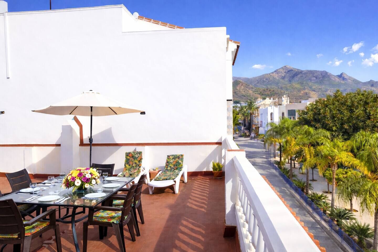 Un espacio de comedor al aire libre con una mesa preparada para dos, sillas y una sombrilla.