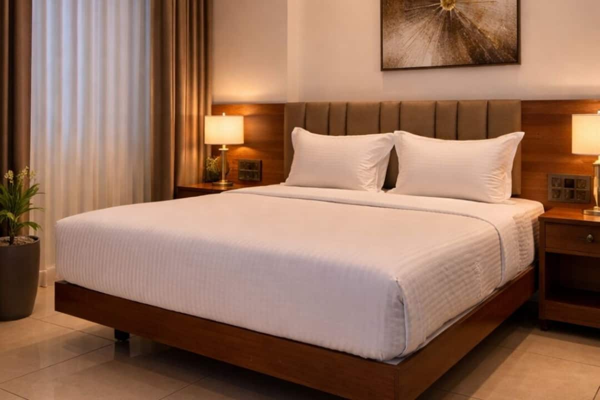 Hotellihuone, jossa on suuri sänky, kaksi yöpöytää, yölamppu, ruukkukasvi ja seinälle ripustettu taideteos.