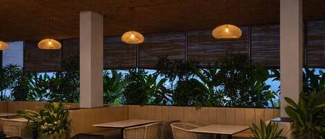 An outdoor seating area with tables and chairs, surrounded by potted plants and a view of the sky.