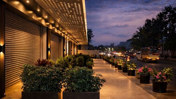 A building with a row of potted plants and a closed shutter door.