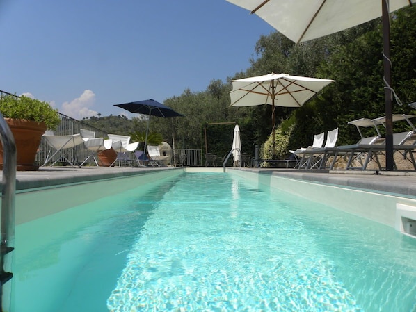 Ein klares Schwimmbecken mit Liegestühlen und Sonnenschirmen darum.