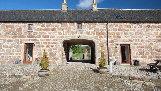 A stone building with a central archway, stone walls, and a cobblestone ground. - Ayrshire Cottage at The Dairy at Daviot (Inverness)