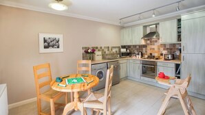 A kitchen with wooden chairs, a dining table, a washing machine, and a microwave. - Ayrshire Cottage at The Dairy at Daviot (Inverness)