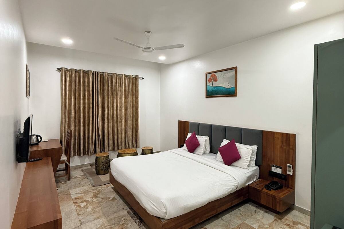 A modern hotel room with a large bed, a desk, a chair, a television, a painting, and a telephone.