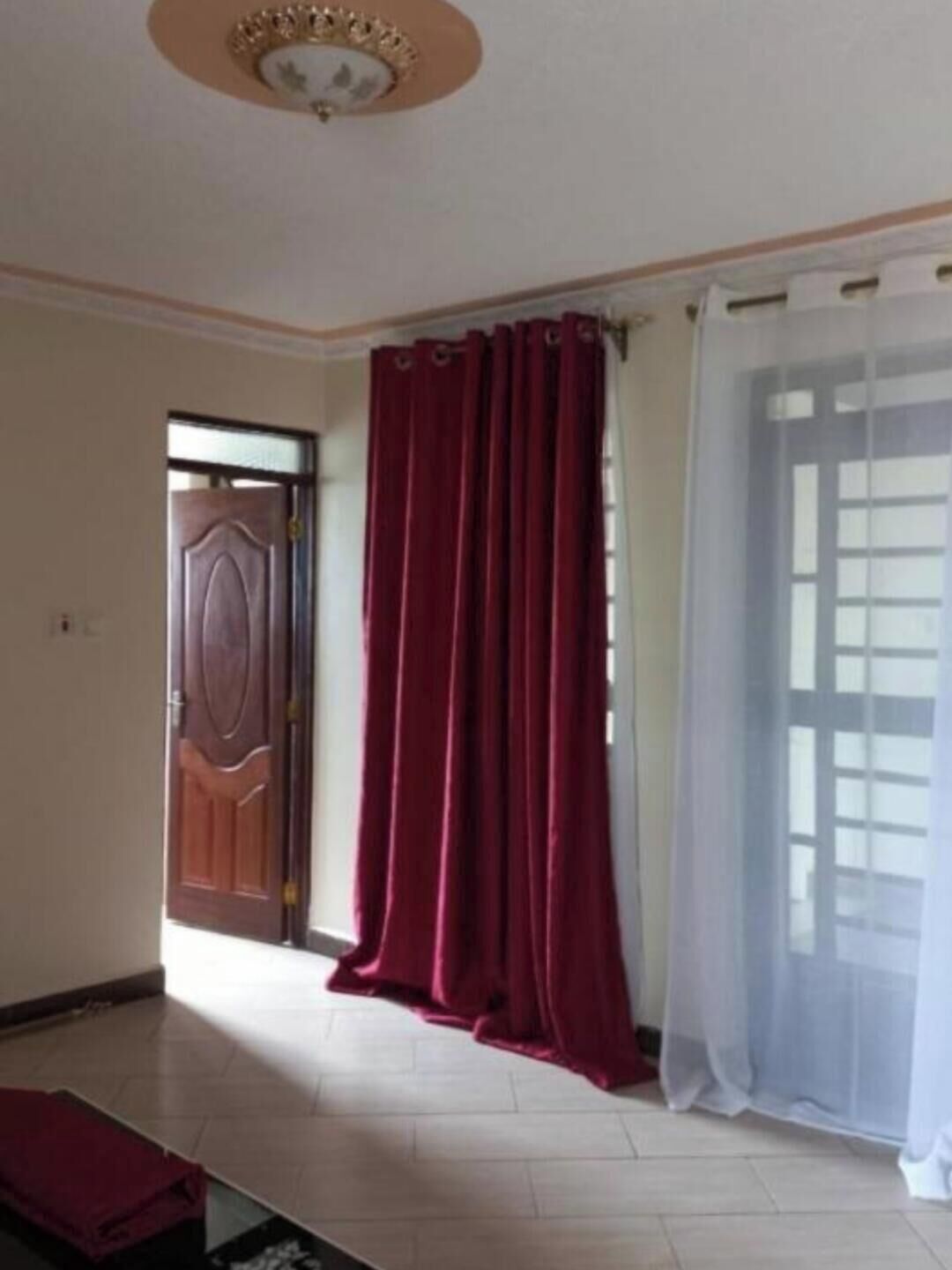 Une pièce avec une porte en bois, un rideau rouge, un rideau blanc et un sol carrelé.
