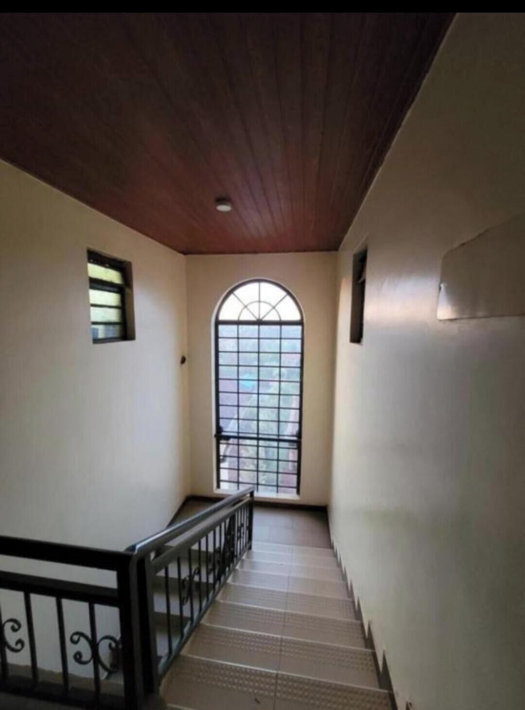 Un escalier avec un plafond en bois, une petite fenêtre et une rampe en métal.