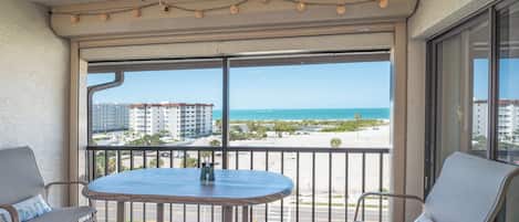 A balcony with a table and chairs, overlooking a beach and buildings.