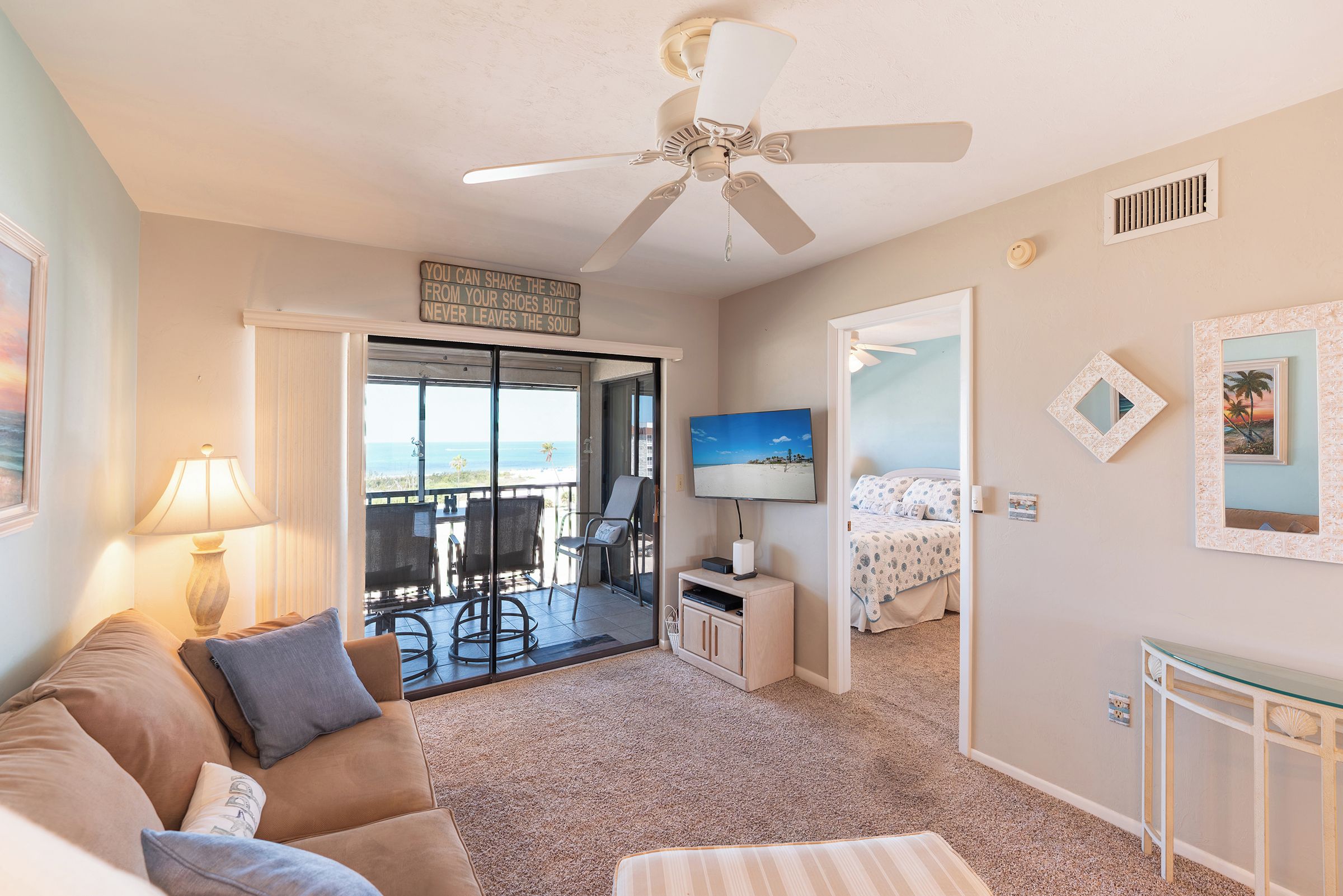 Ein Hotelzimmer mit Balkon, Deckenventilator, Fernseher und einem Bett mit Strandmotiv.
