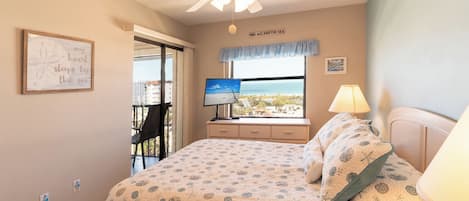 Un dormitorio con cama, escritorio con computadora, ventana con vista y ventilador de techo.