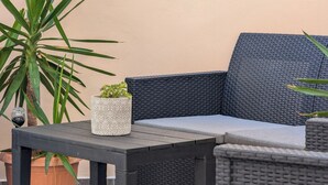 Un conjunto de sofá y mesa de mimbre frente a una pared, con una planta en maceta y un objeto decorativo sobre la mesa.