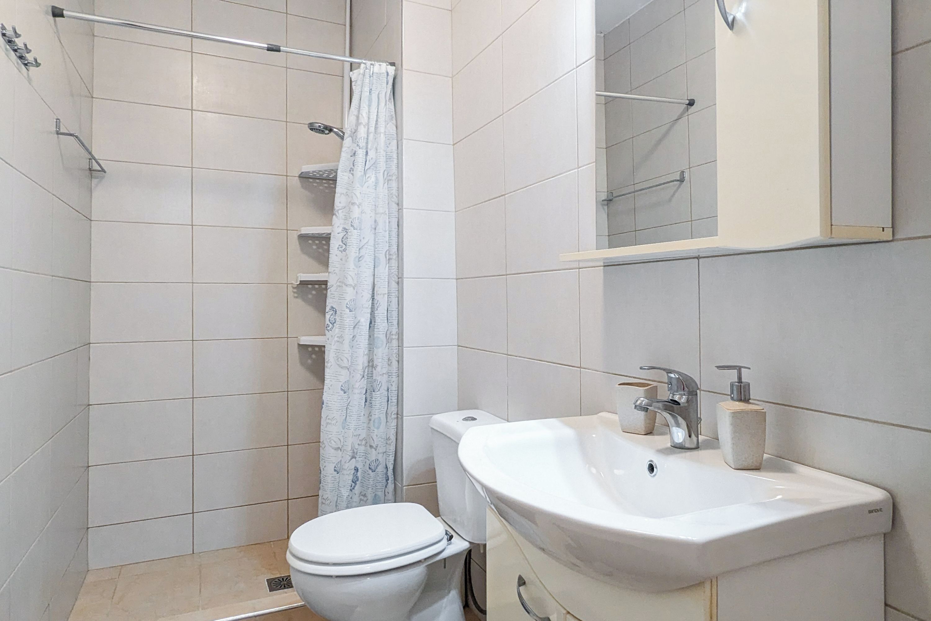 Een badkamer met toilet, een douche met gordijn, wastafel met spiegel en een zeepdispenser.