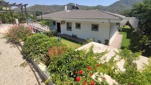 Ein zweistöckiges Haus mit einem Ziegeldach, einer Veranda und einem Garten mit verschiedenen Pflanzen und Blumen.