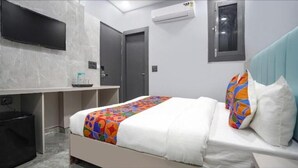 A hotel room with a bed, a TV mounted on the wall, a desk, and an air conditioning unit. - Staylo The Royal  (New Delhi)