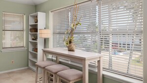 Ein Zimmer mit weißem Tisch, zwei Bänken, einer Vase mit Zweigen, einer Lampe und Regalen mit Körben.