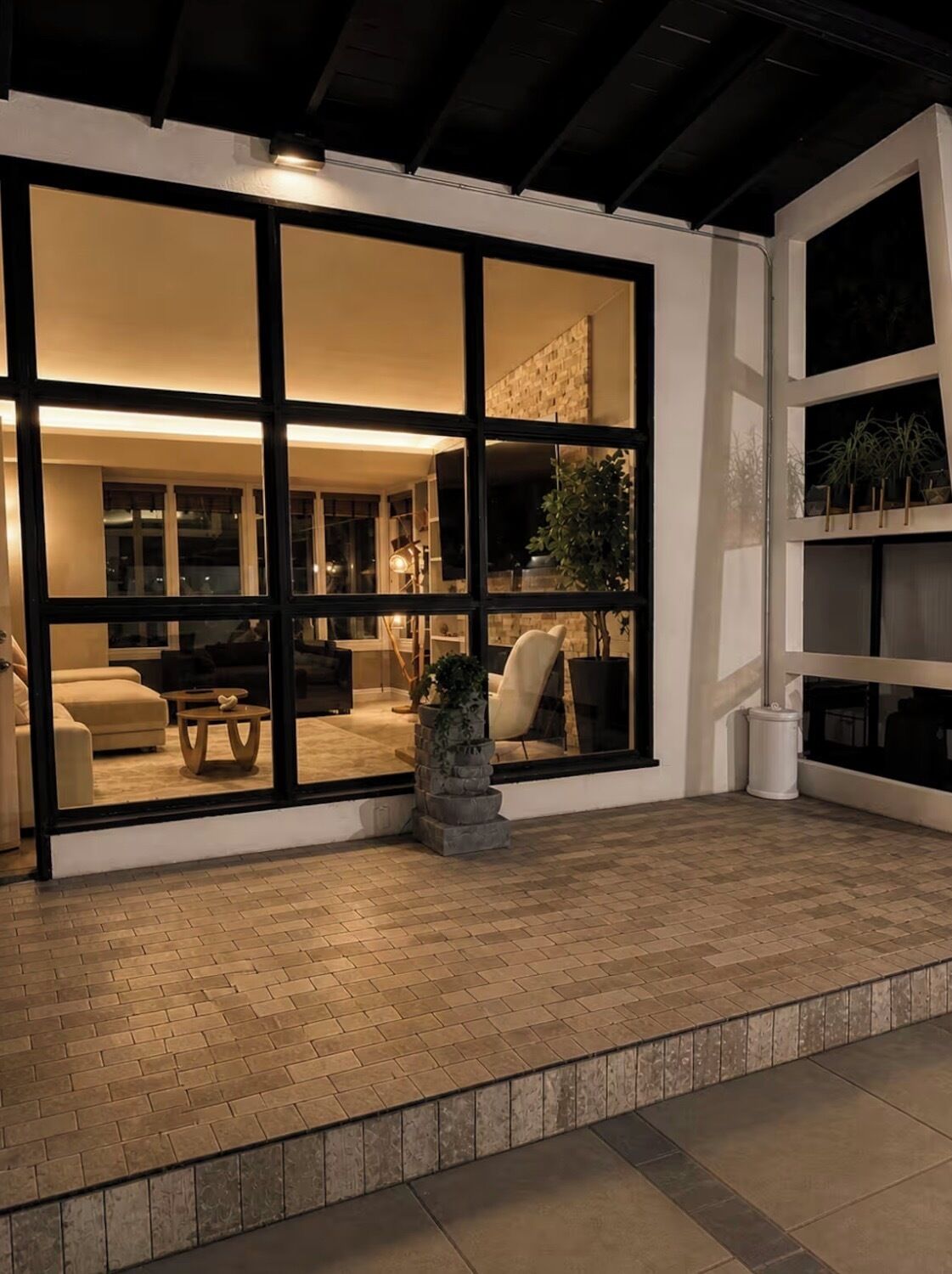 A modern interior with a large glass door leading to a living area with a sofa, coffee table, and a potted plant.