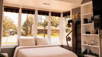 Un dormitorio con una cama, una mesa redonda, un televisor y una ventana con cortinas.