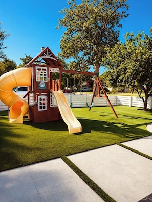 A playground with a slide and swings, surrounded by a well-maintained lawn and trees.