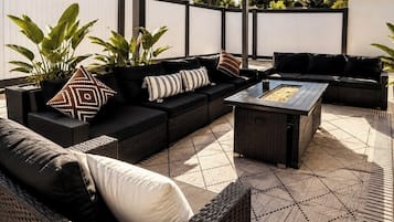 Un patio al aire libre con mobiliario de mimbre, incluyendo sofás y una mesa de centro, y plantas en macetas.