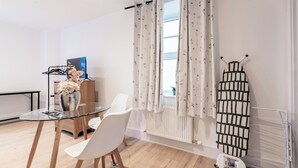 Une pièce moderne avec une table en verre, des chaises blanches, un radiateur et un étendoir.