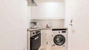 Une cuisine compacte équipée d’un four encastré, d’un lave-linge et d’un petit plan de travail sur lequel se trouvent une bouilloire et une bouteille.