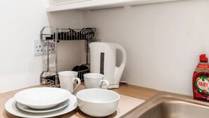 Une cuisine avec des meubles blancs, un évier en acier inoxydable, une bouilloire, un égouttoir et une bouteille de liquide vaisselle de la marque Fairy.