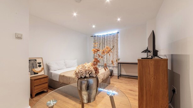 Une chambre d’hôtel moderne, équipée d’un lit, d’une petite table avec un vase, d’une télévision et d’une armoire en bois.