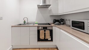 Una cocina compacta con alacenas blancas, una campana extractora de acero inoxidable, horno empotrado, microondas y un lavamanos con escurreplatos.