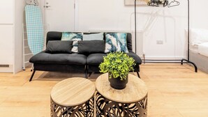 Un salón moderno con un sofá negro, dos mesas redondas de madera, una planta en maceta y un radiador.