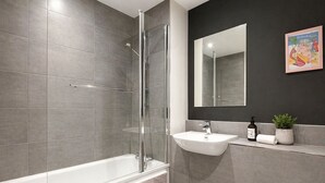 A modern bathroom with a glass-enclosed shower, a white sink, and a dark wall. - Modern Riverside Apartment | Balcony | Elizabeth Line (London)